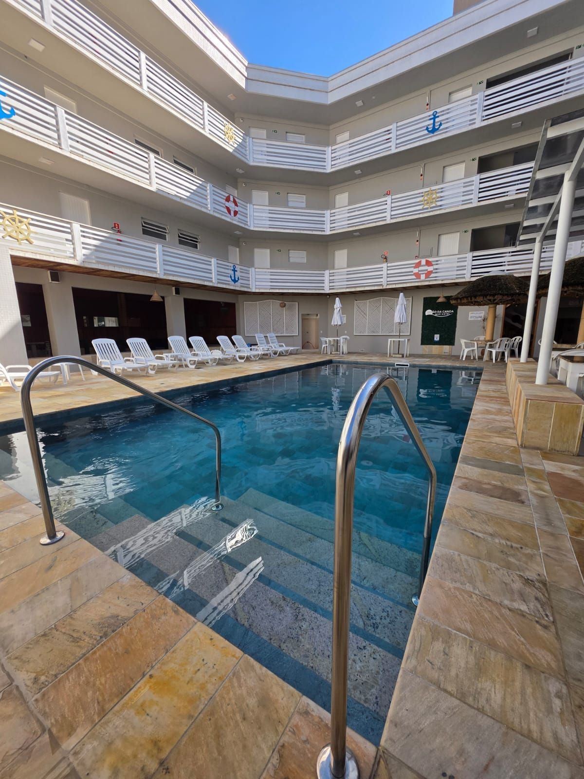 Piscina coberta de hotel com água azul, corrimãos de metal e varandas em vários níveis ao redor