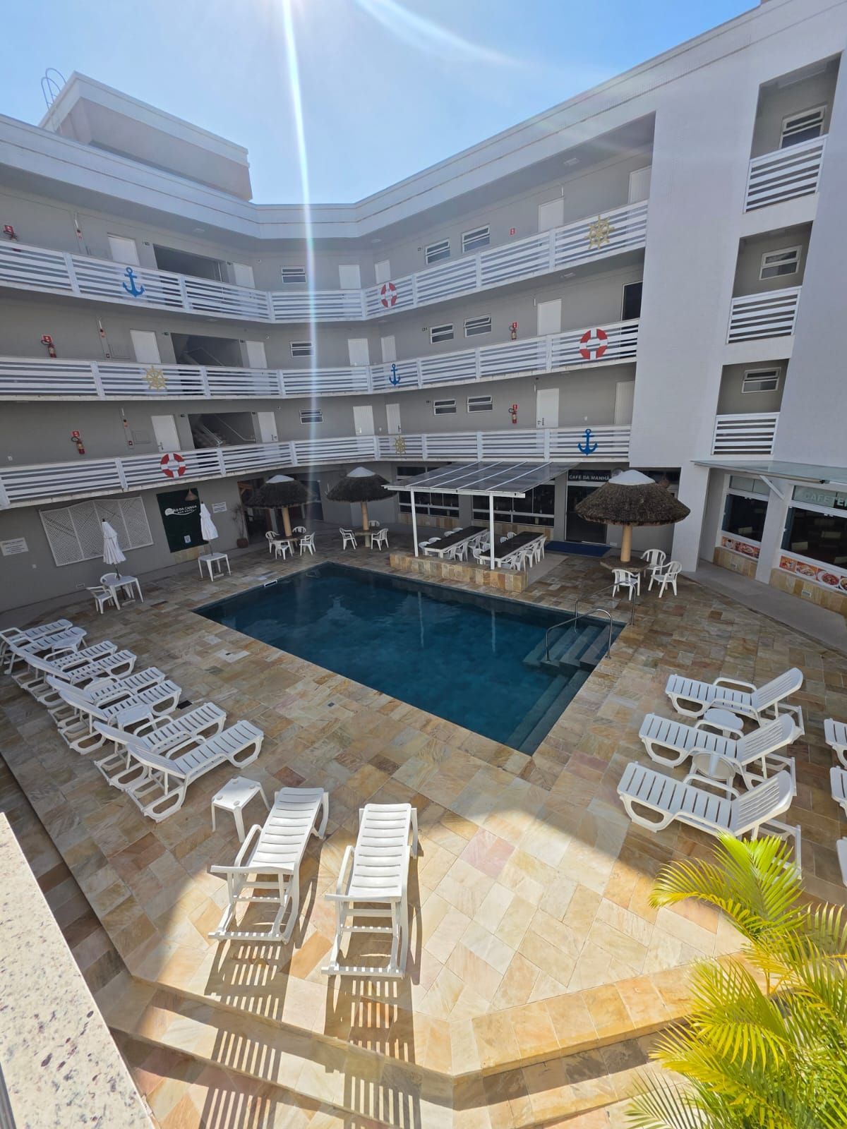 Piscina de hotel Courtyard rodeada por espreguiçadeiras brancas e varandas sob o sol forte