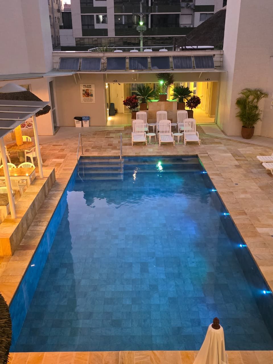 Piscina iluminada num lounge no pátio, com cadeiras brancas e uma iluminação ambiente acolhedora ao anoitecer