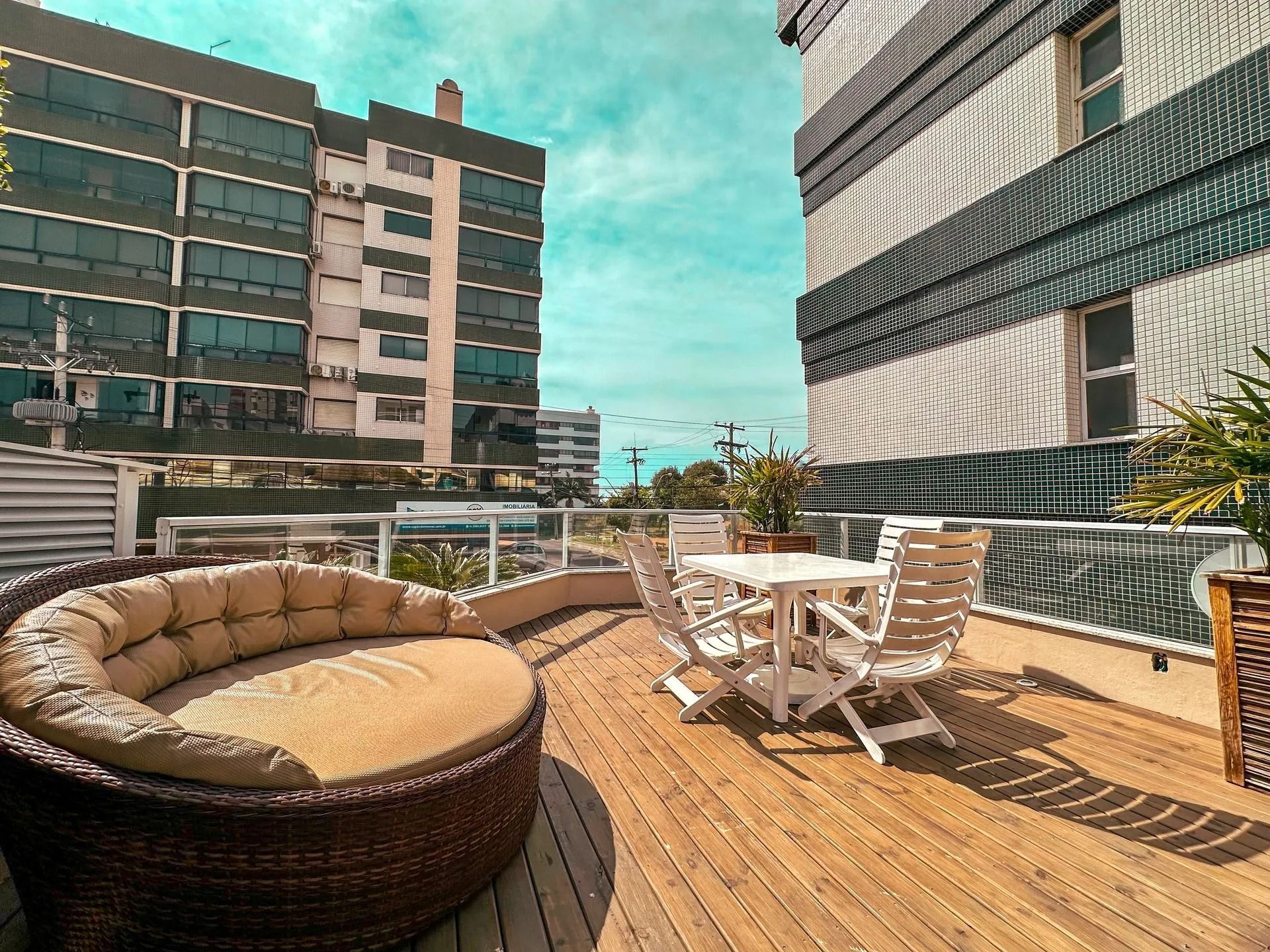 Terraço no rooftop com móveis de vime, mesa e cadeiras brancas e prédios da cidade sob um céu azul