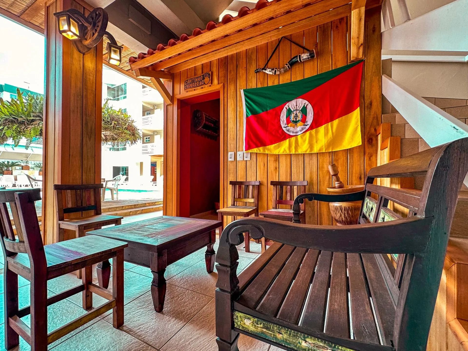 Pátio de madeira ao ar livre com mesas, cadeiras e uma bandeira vermelha, verde e amarela pendurada na parede