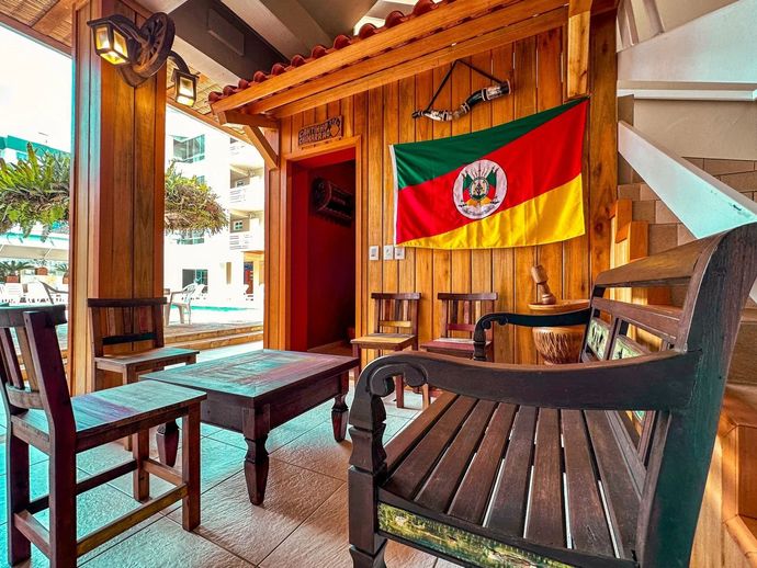 Área de estar de madeira na varanda, com uma bandeira vermelha e verde pendurada na parede, perto da porta aberta