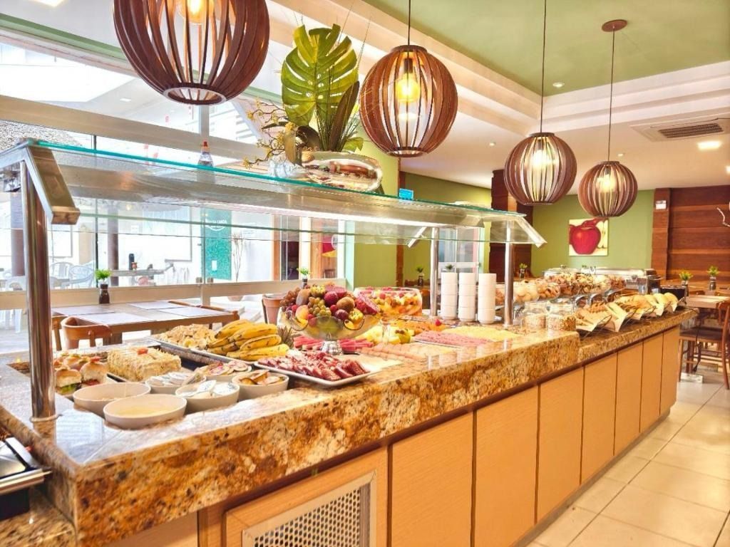 Balcão de buffet com várias opções de café da manhã sob luminárias suspensas, em um restaurante bem iluminado