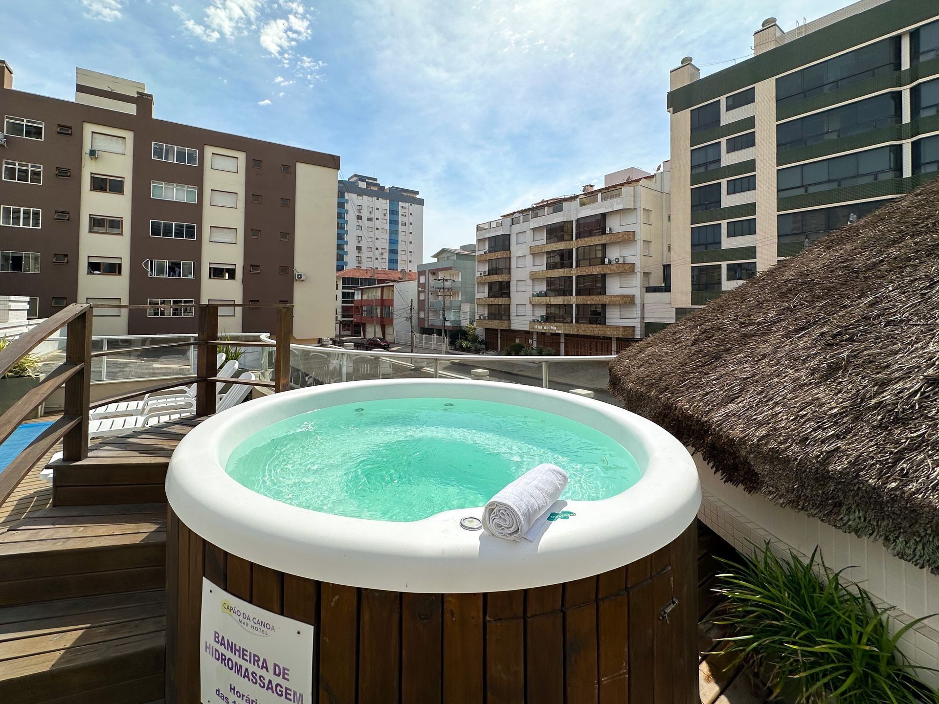 Banheira de hidromassagem no terraço com água turquesa, rodeada por prédios residenciais sob um céu azul.