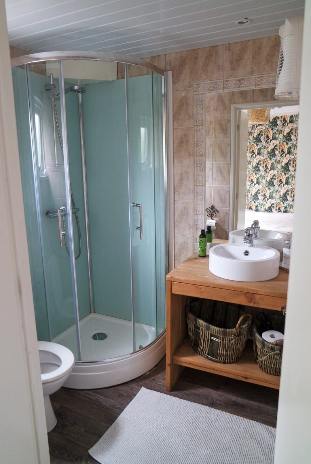 Badkamer met een blauwe douche, een houten wastafelmeubel en een ronde wasbak.