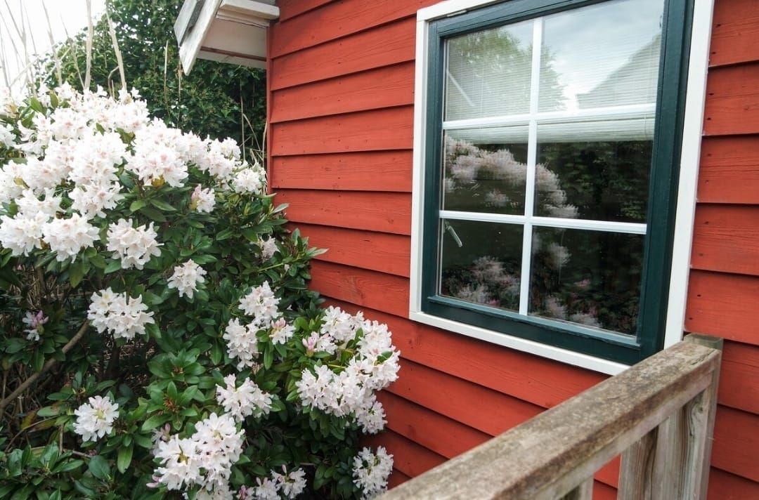 Een huis met rode gevelbekleding, een raam, witte bloemen ervoor en een houten balustrade.