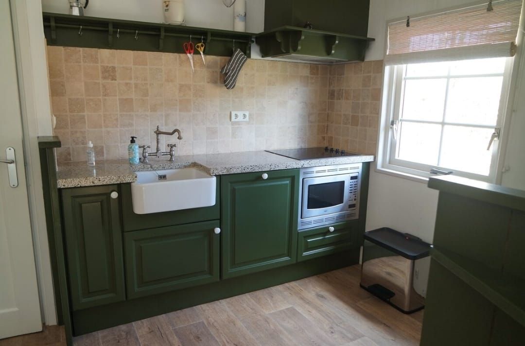 Groene keuken met een boerenkeuken spoelbak, betegelde achterwand en magnetron.