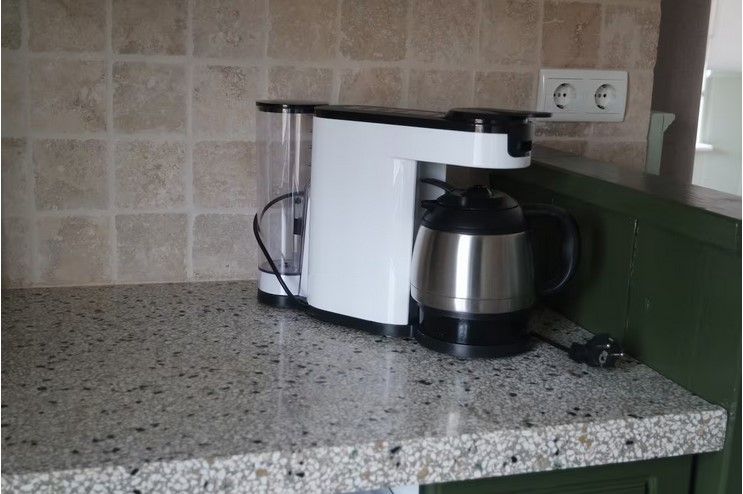 Een koffiezetapparaat op een gespikkeld aanrechtblad voor een betegelde achterwand, naast een groene kast en een stopcontact.