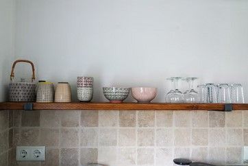 Houten plank met servies en glazen boven een betegelde achterwand.