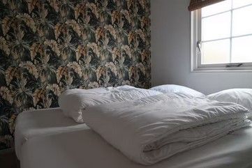 Een bed met wit beddengoed en een muur met een patroon in een kamer met een raam.