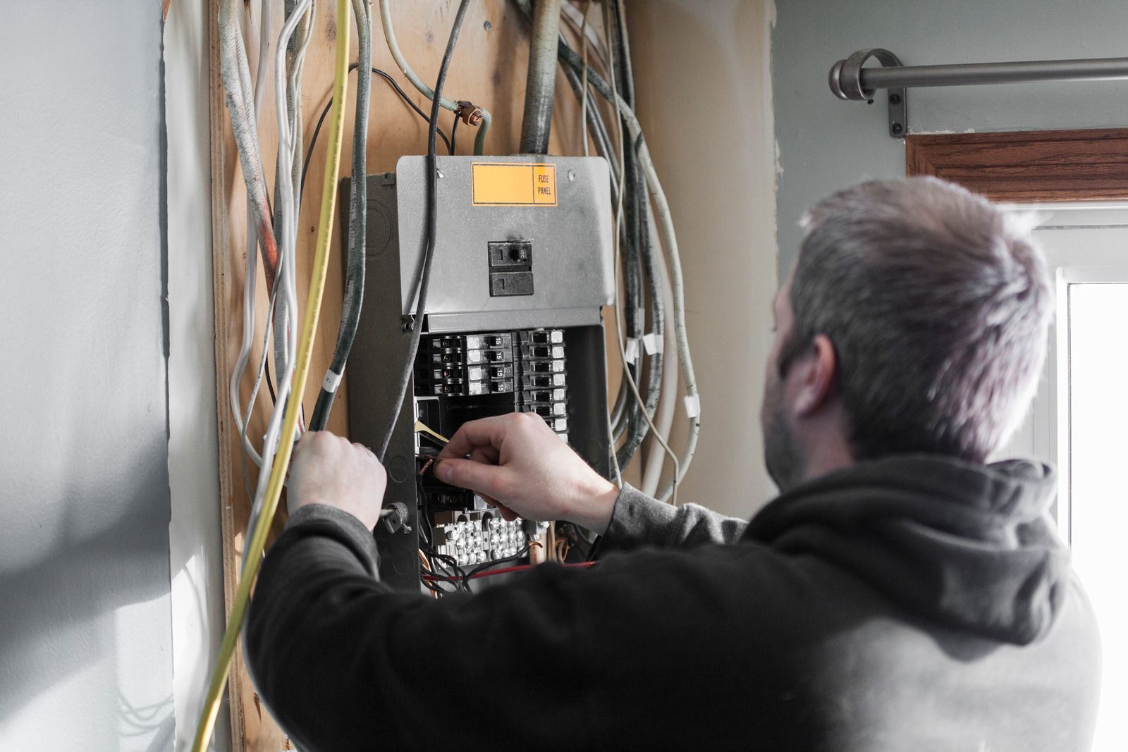 A man is working on an electrical panel on a wall.
