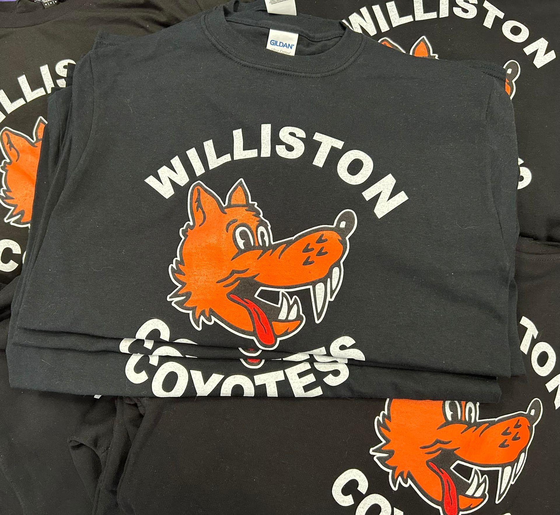Stacked black Williston Coyotes T-shirts with orange fox logo and white text