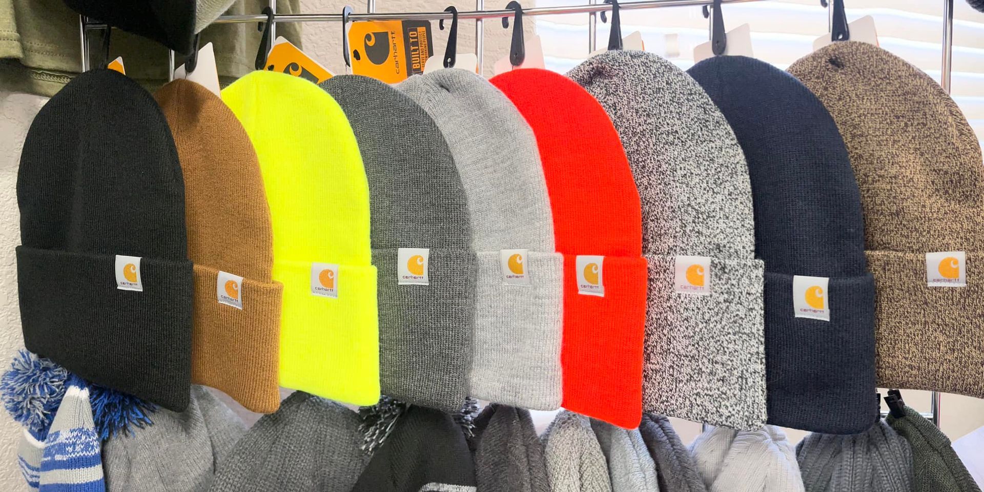 Row of colorful knitted beanies in black, brown, neon yellow, gray, red, and navy on display stands