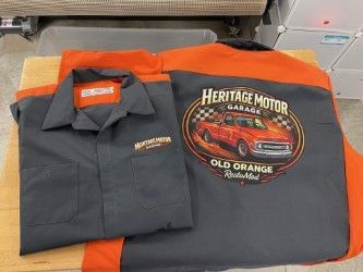 Folded gray and orange Heritage Motor Garage shirts displayed on a shelf with logo and branding visible
