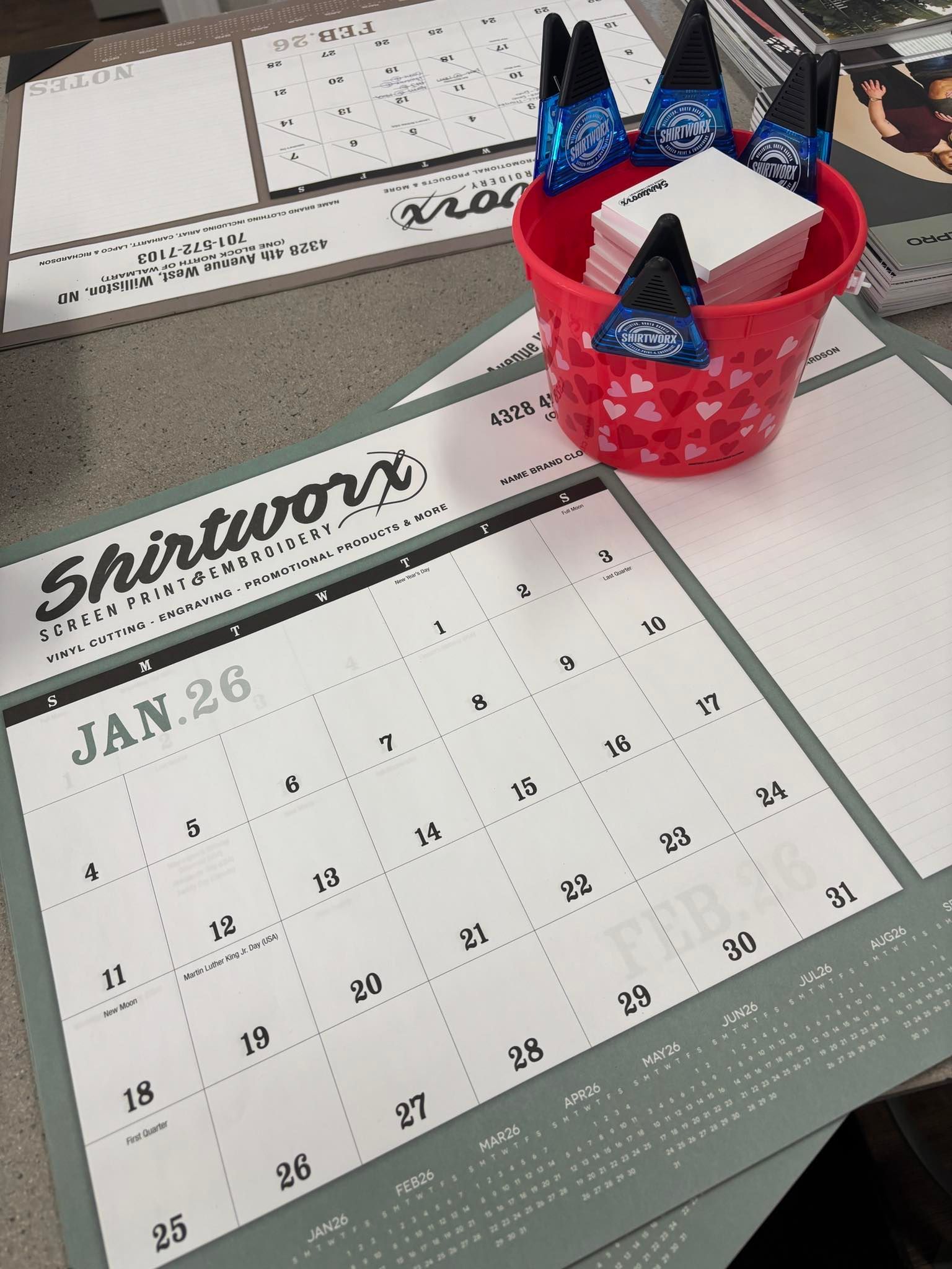 Calendar page on a desk with a red basket holding blue-starred folded notes and a keyboard nearby