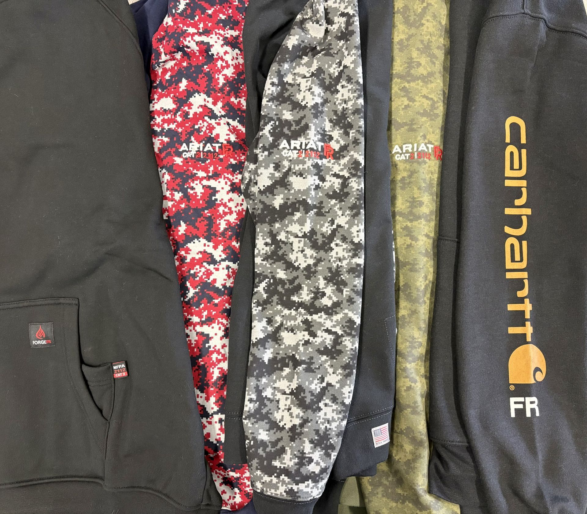Four folded hoodies and sweatpants in black, red camo, gray camo, and black with yellow lettering.