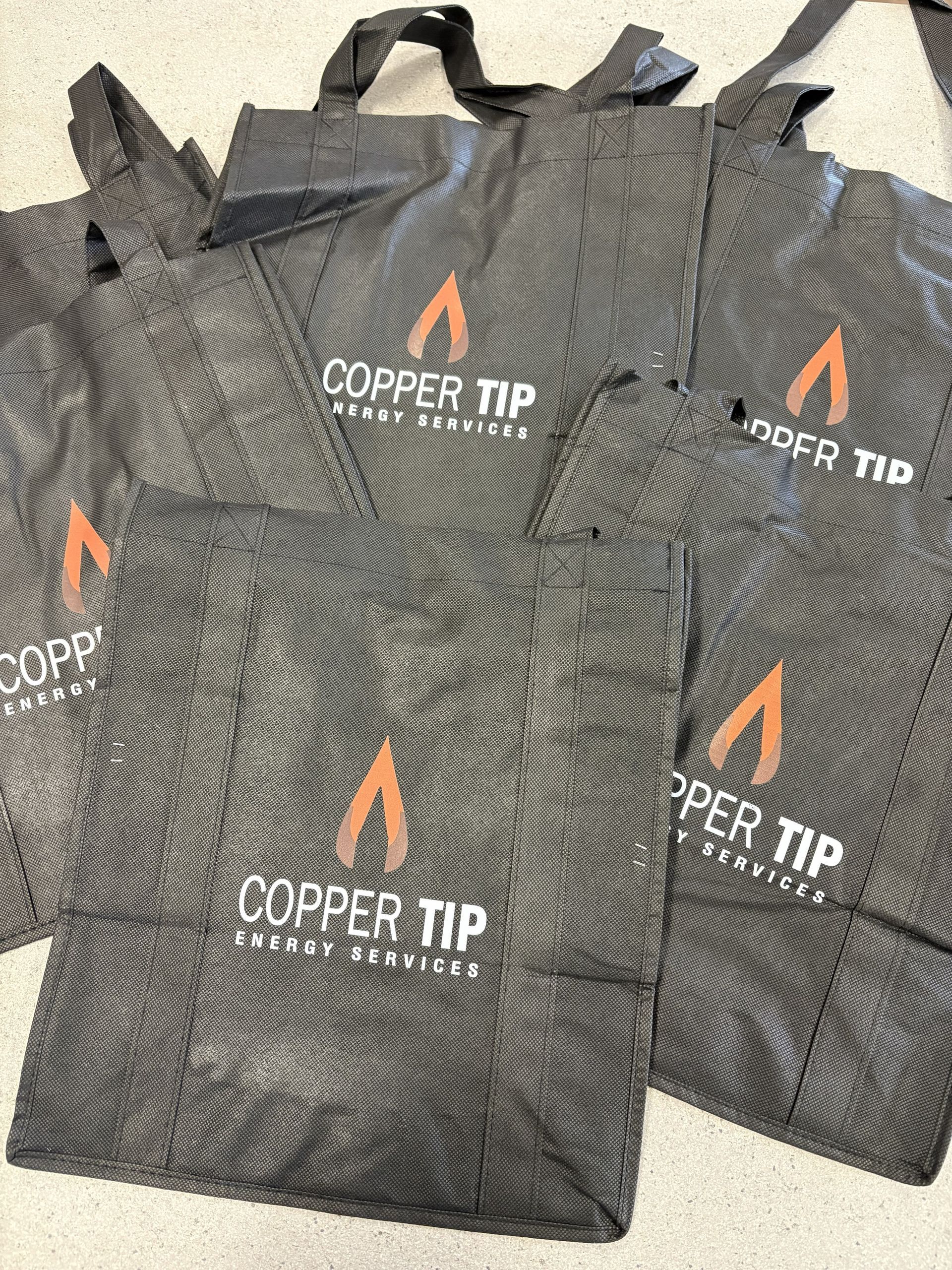 Black COPPER TIP reusable tote bags with orange logo stacked together