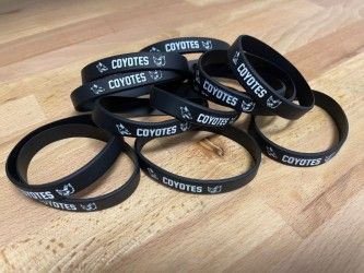 Stacked black wristbands with white “COYOTES” text on a wooden surface
