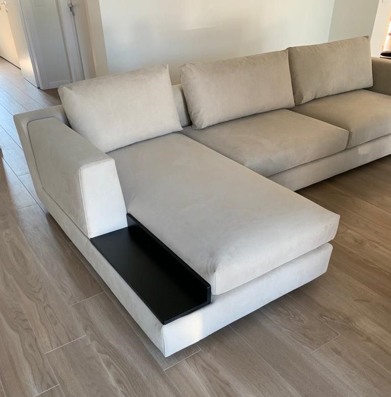 Divano componibile beige con tavolino laterale scuro incorporato in una stanza con pavimenti in legno.