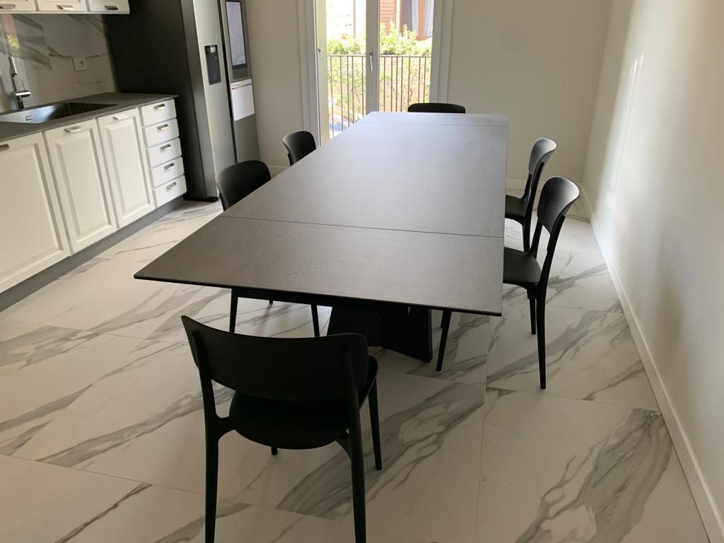 Una sala da pranzo con un lungo tavolo nero e sei sedie nere.
