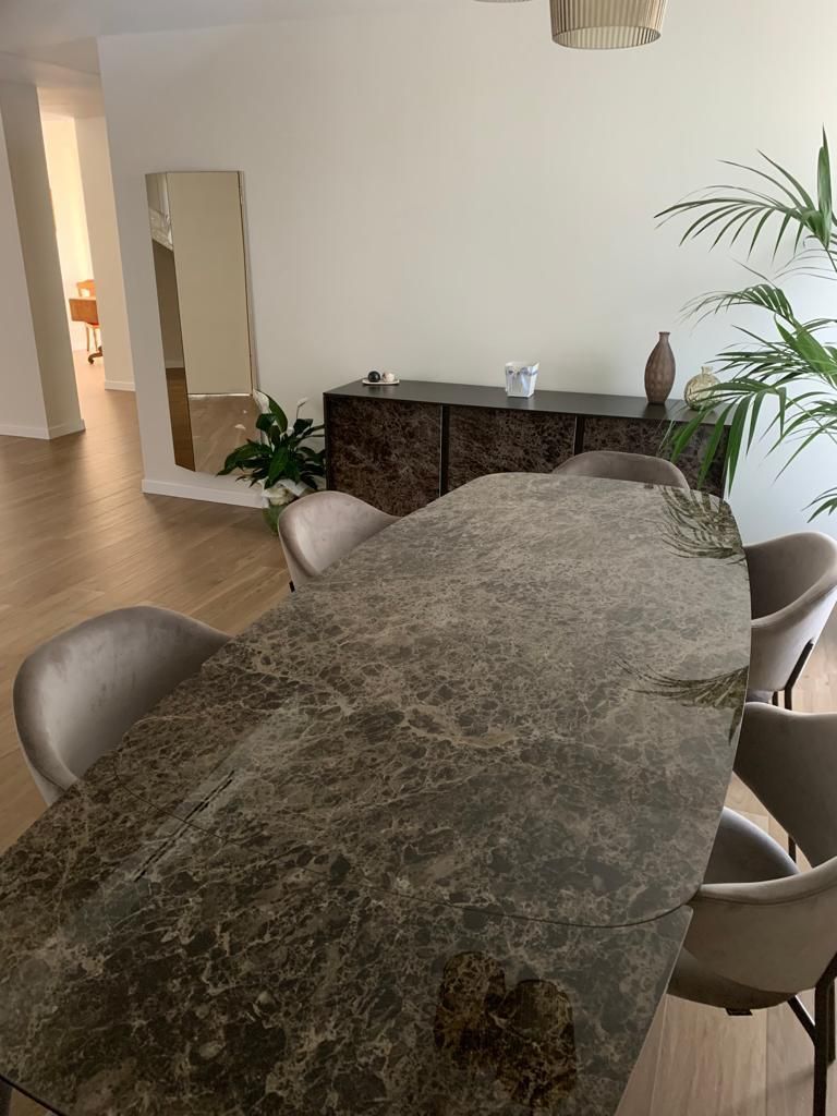 Sala da pranzo con tavolo in pietra, sedie beige, una credenza in legno scuro e piante.