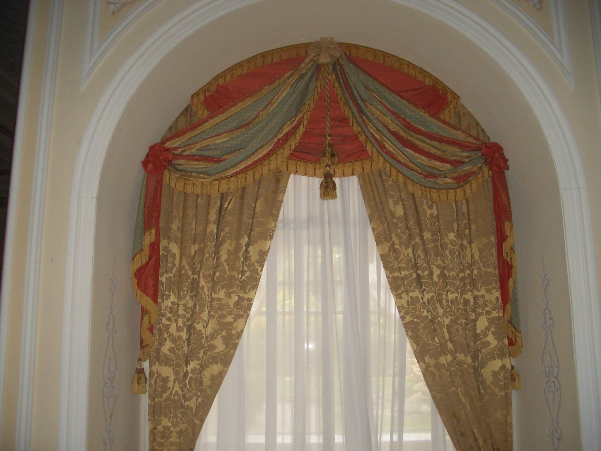 Tende ornate color oro e rosso incorniciano una finestra all'interno di una nicchia ad arco.