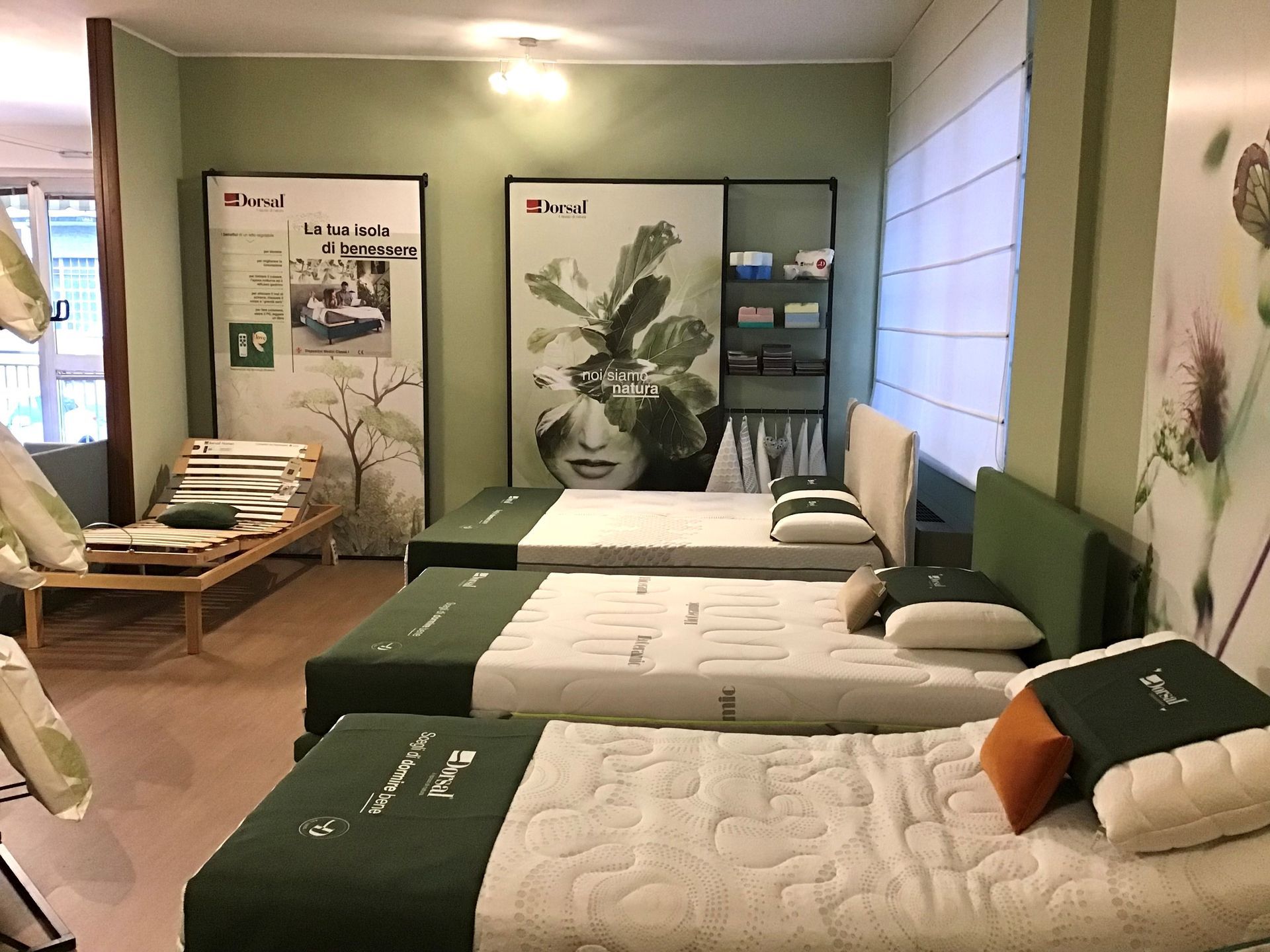 Materassi esposti in uno showroom con una combinazione di colori verde e bianco, poster e strutture per letti in legno.