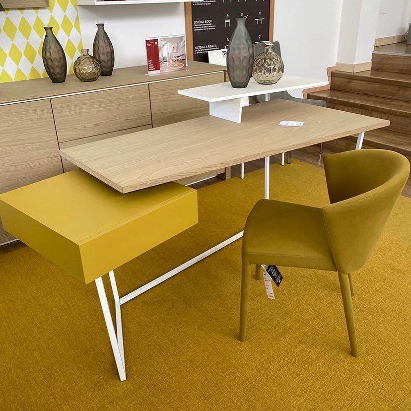 Scrivania moderna con cassetto giallo, sedia e piano in legno chiaro, posta su un tappeto giallo.