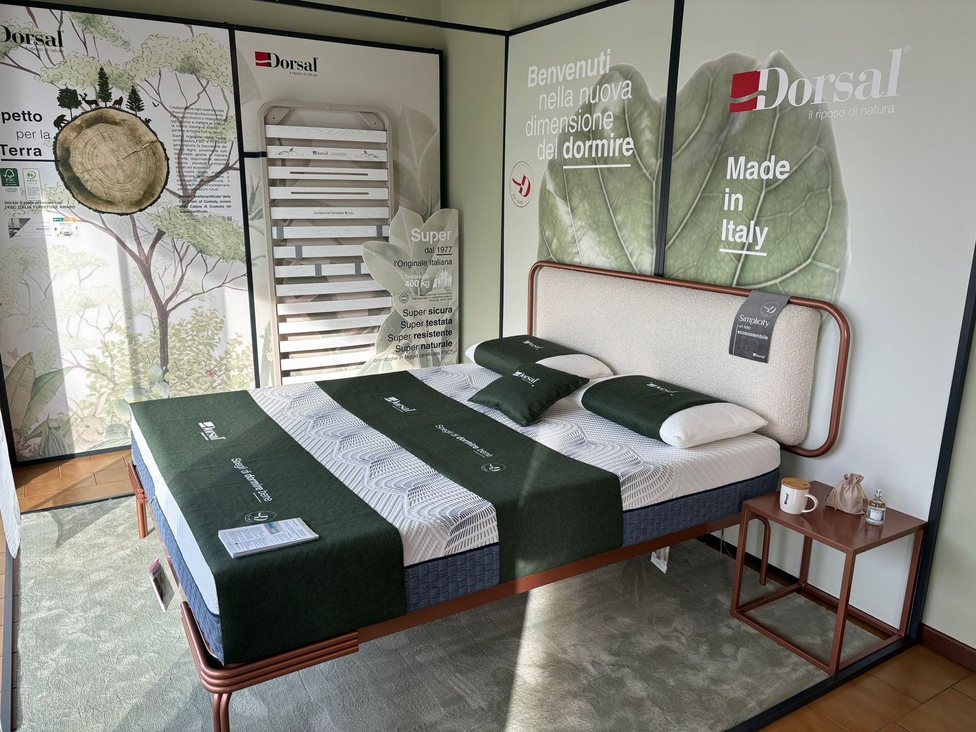 Esposizione di una camera da letto con struttura del letto e materasso, con biancheria da letto verde e bianca.