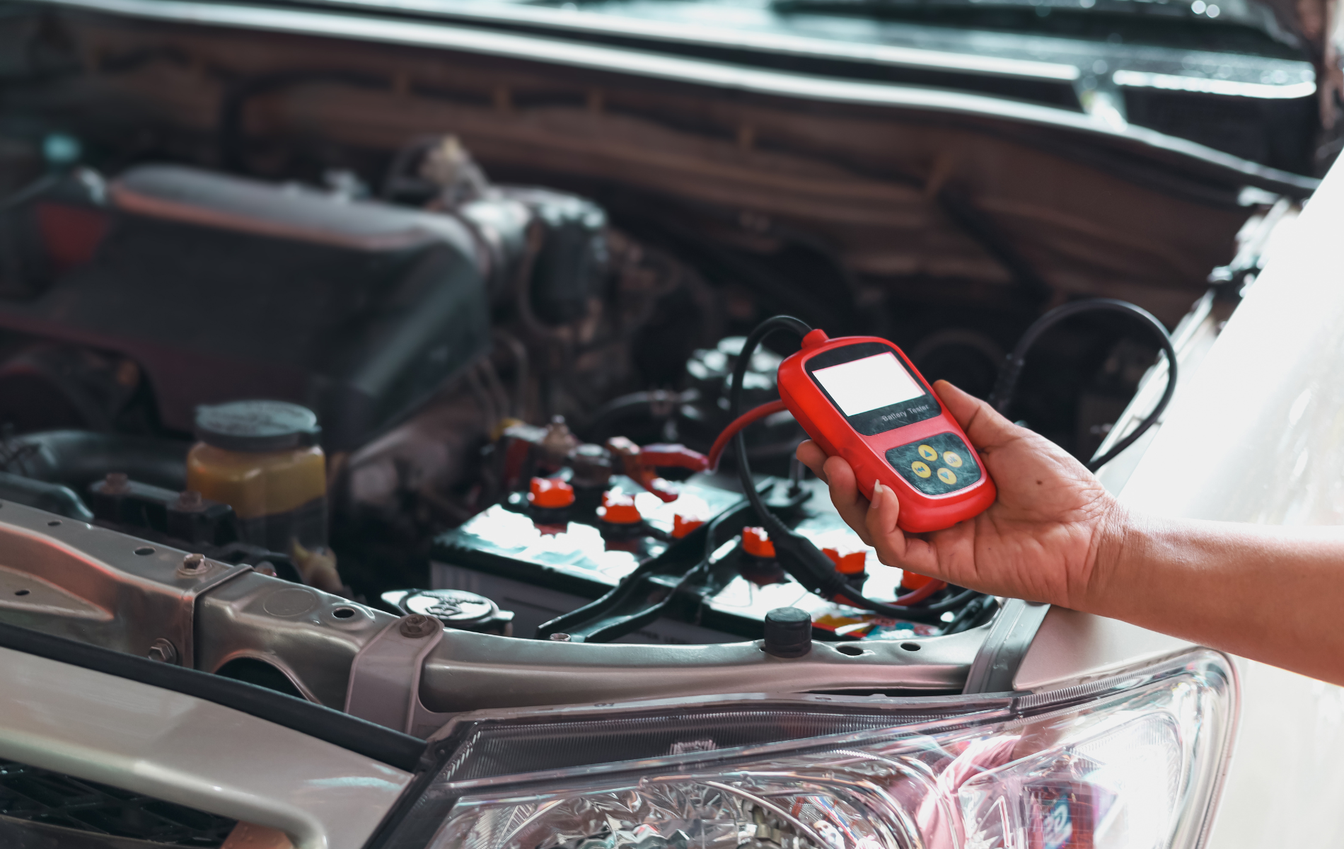 A person is holding a tool in front of a car with the hood open.
