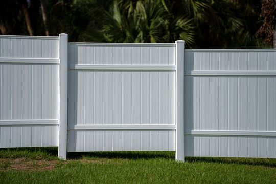 White vinyl fence with three panels and posts along a grassy yard, with palm trees in the background