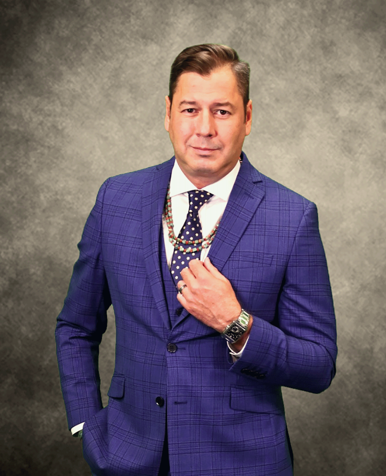 A man in a blue suit and tie is standing with his hands in his pockets.