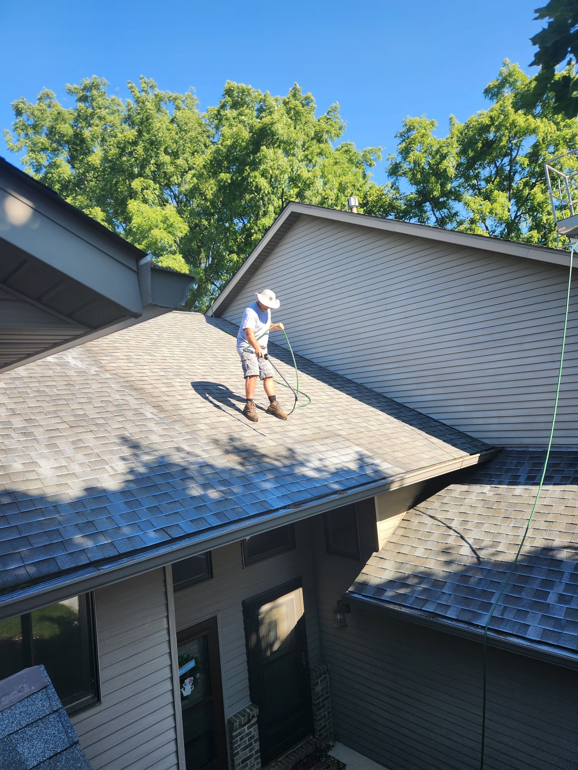 A man is cleaning the roof of a house with a hose