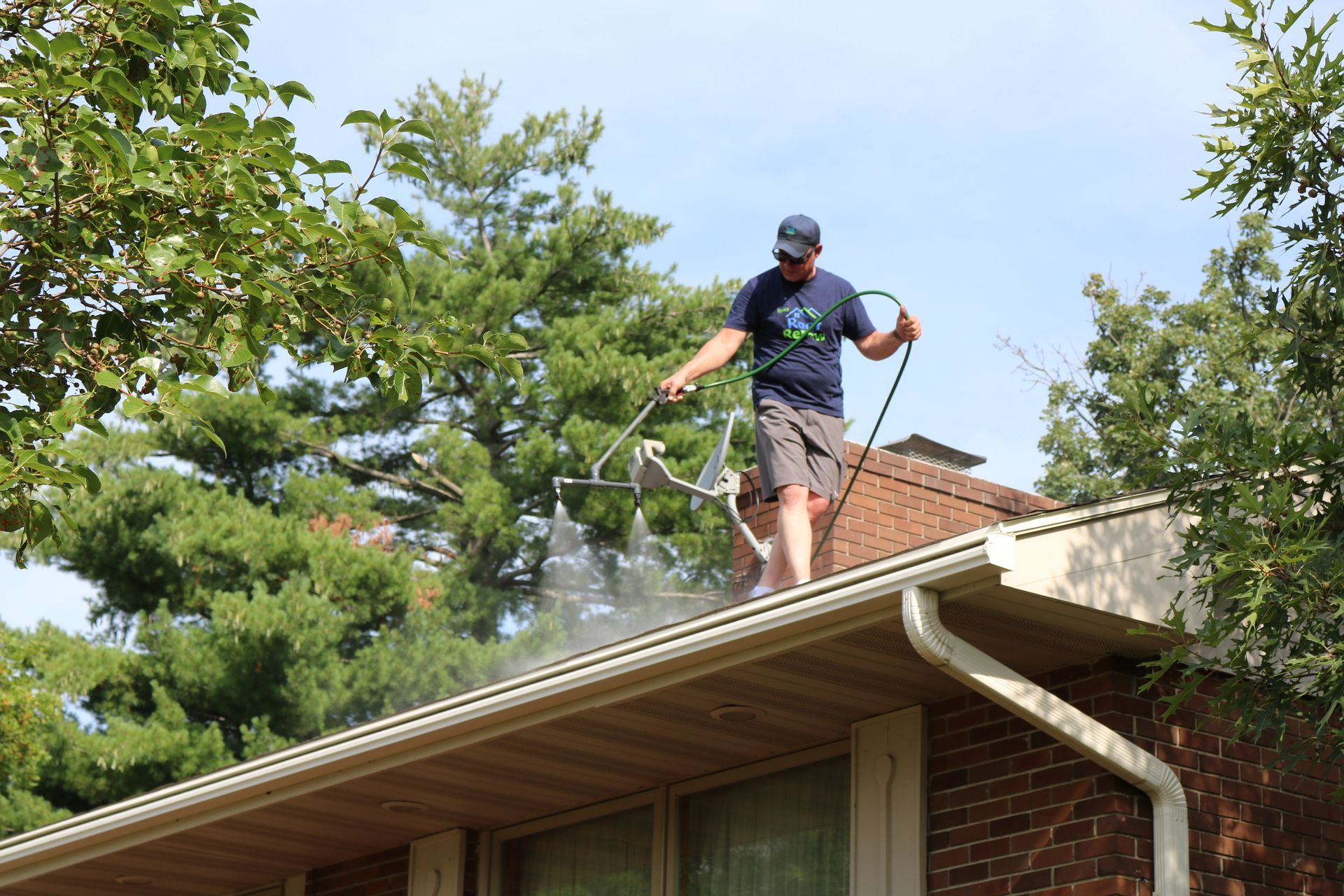 A man is cleaning the roof of a house with a pressure washer.