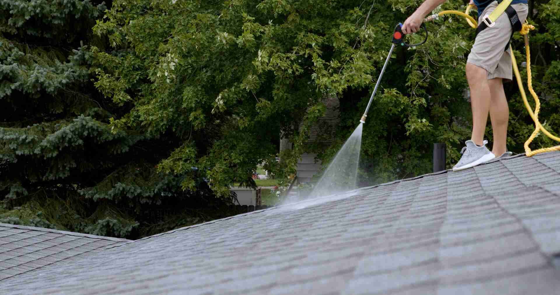A man is cleaning the roof of a house with a high pressure washer.