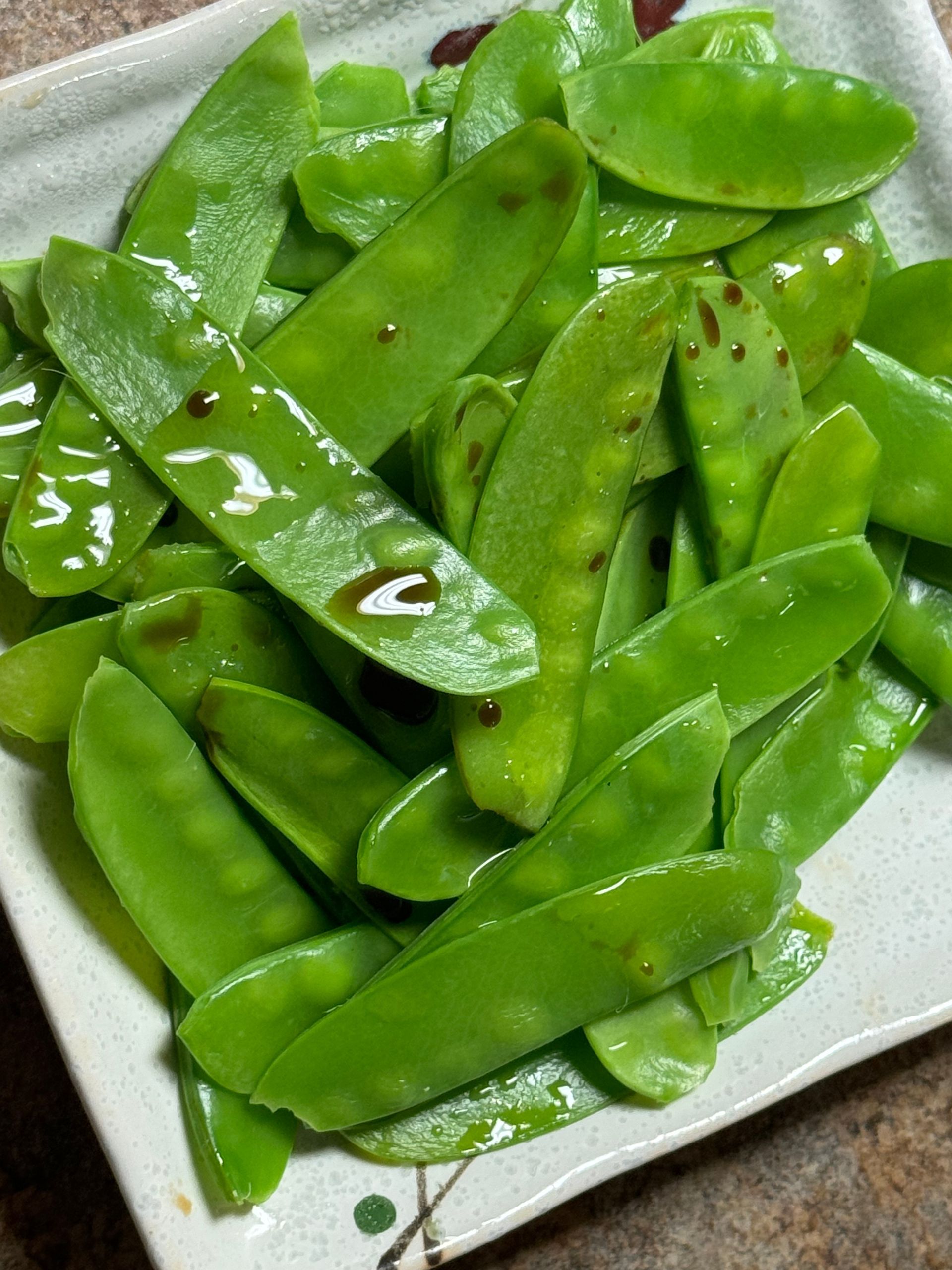 A close up of a plate of green peas on a table.