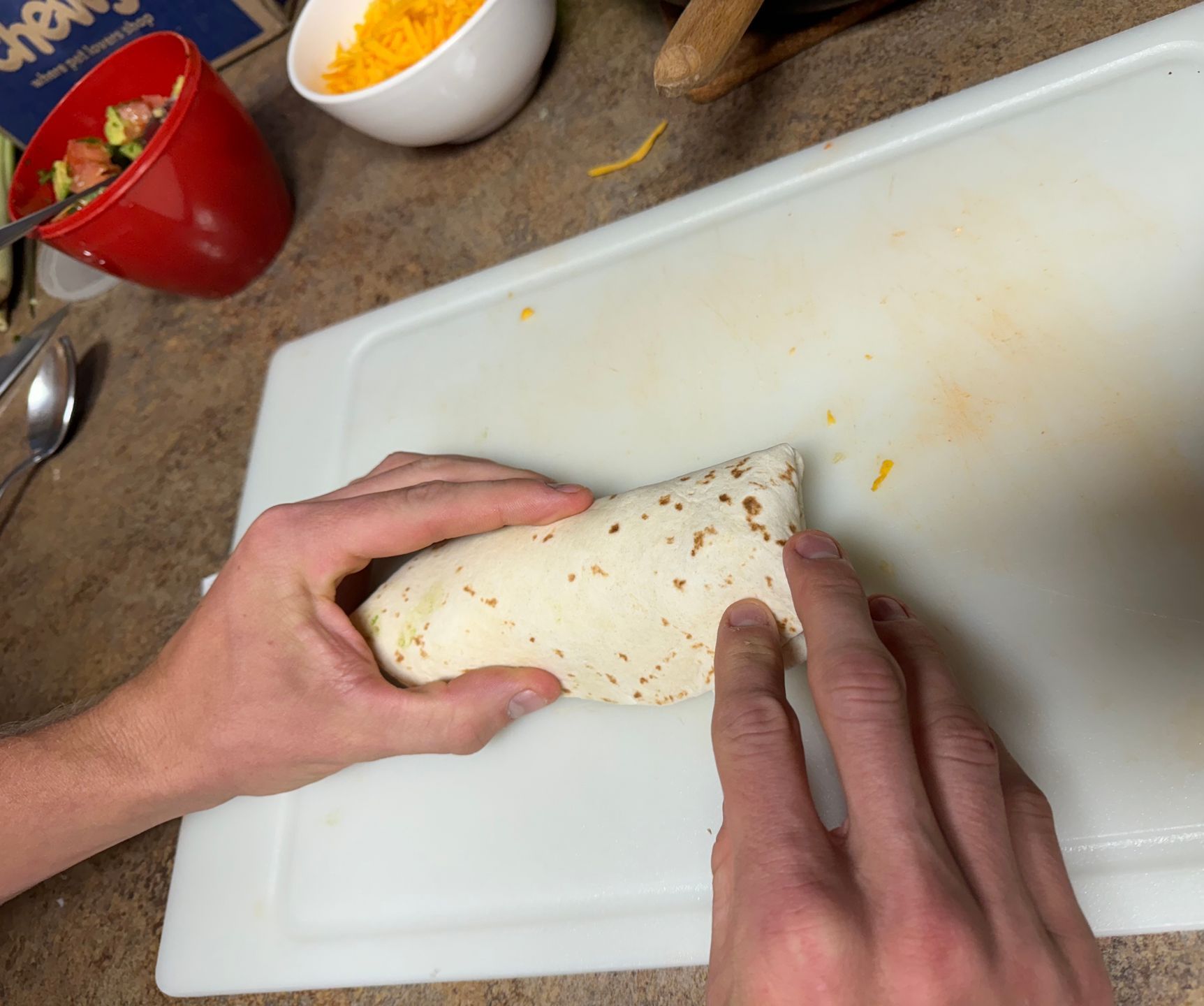 A person is rolling a burrito on a cutting board.