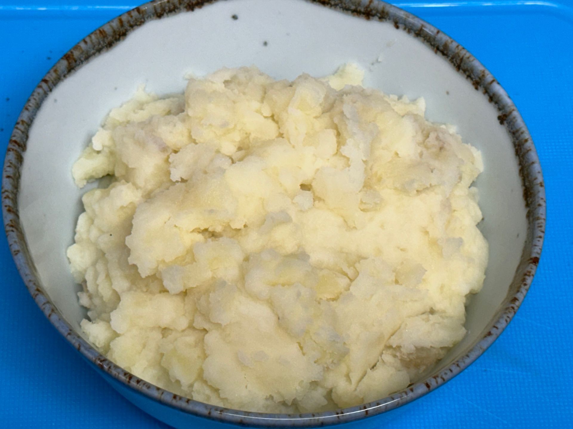 A bowl of mashed potatoes on a blue surface