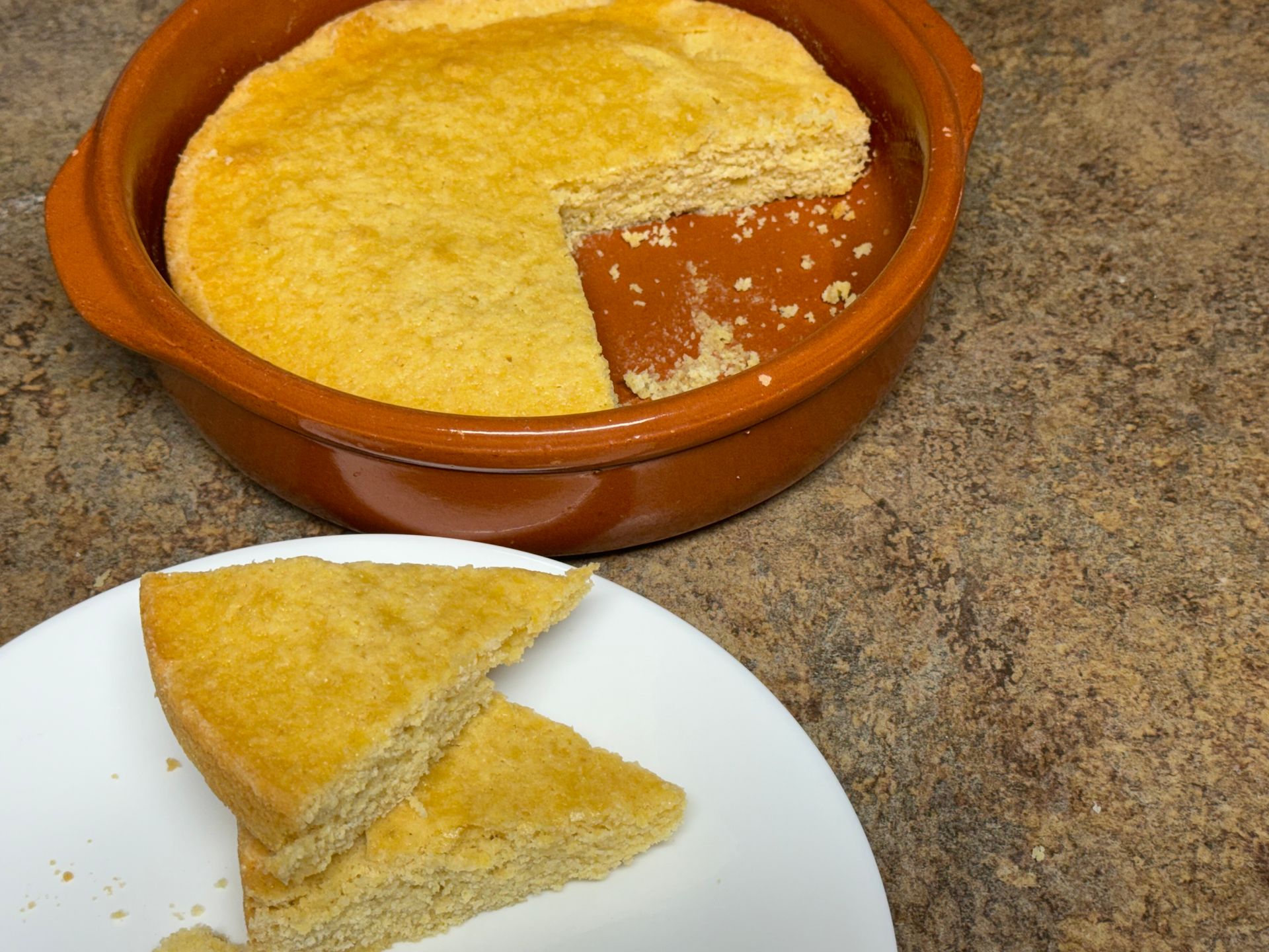 A piece of cornbread is on a plate next to a bowl of cornbread