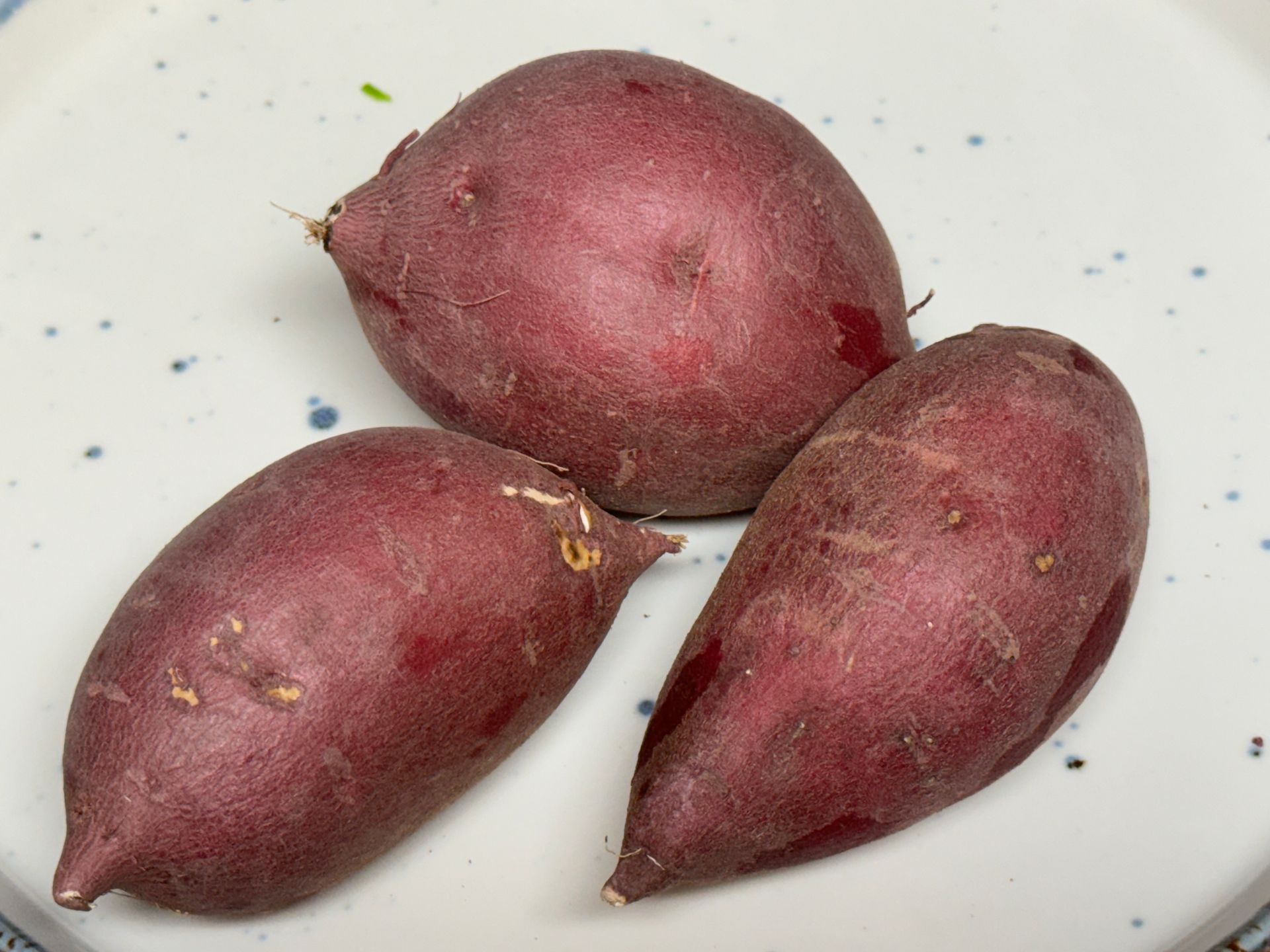 Three purple potatoes are on a white plate
