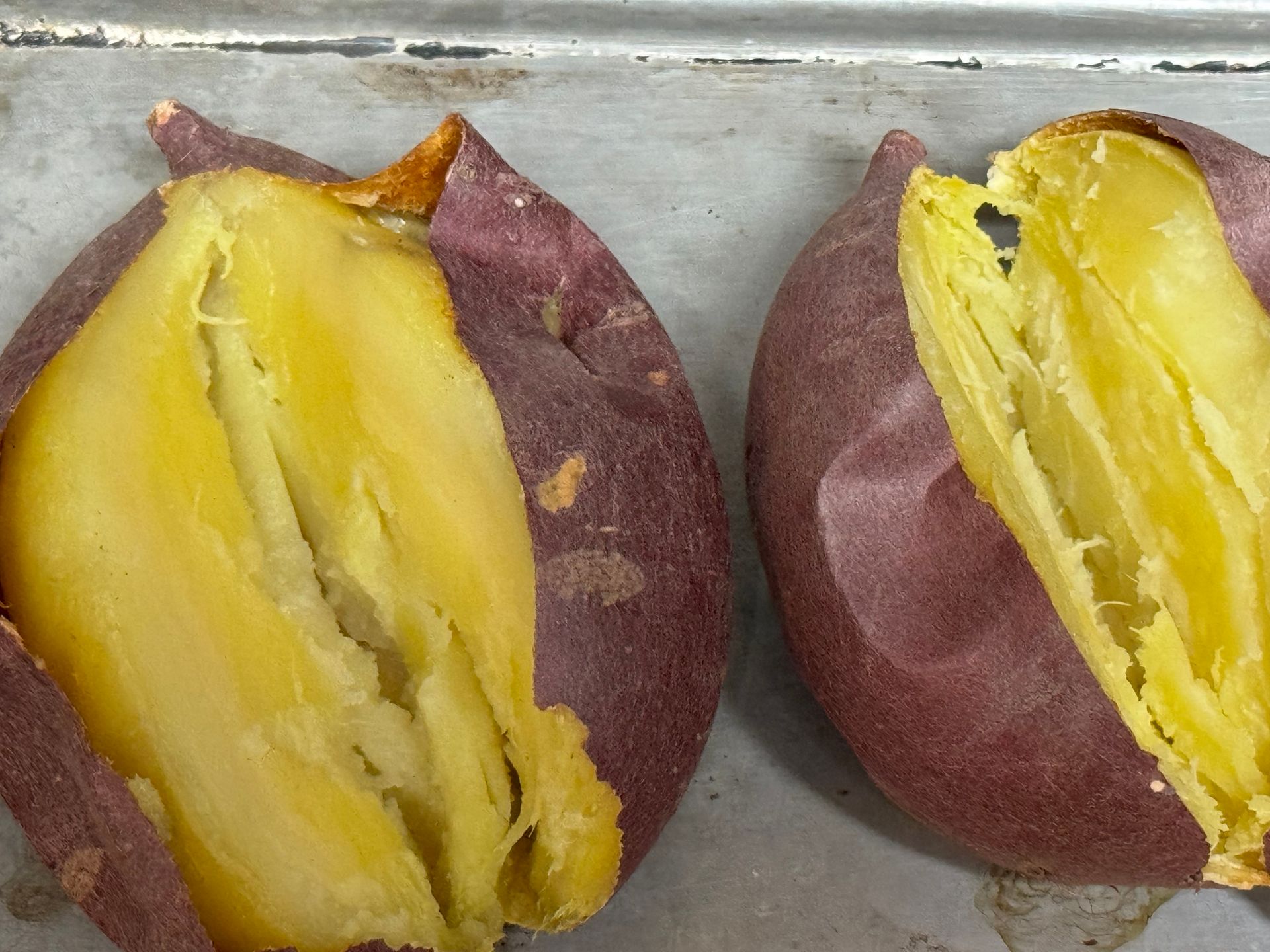 Two baked sweet potatoes are cut in half on a pan