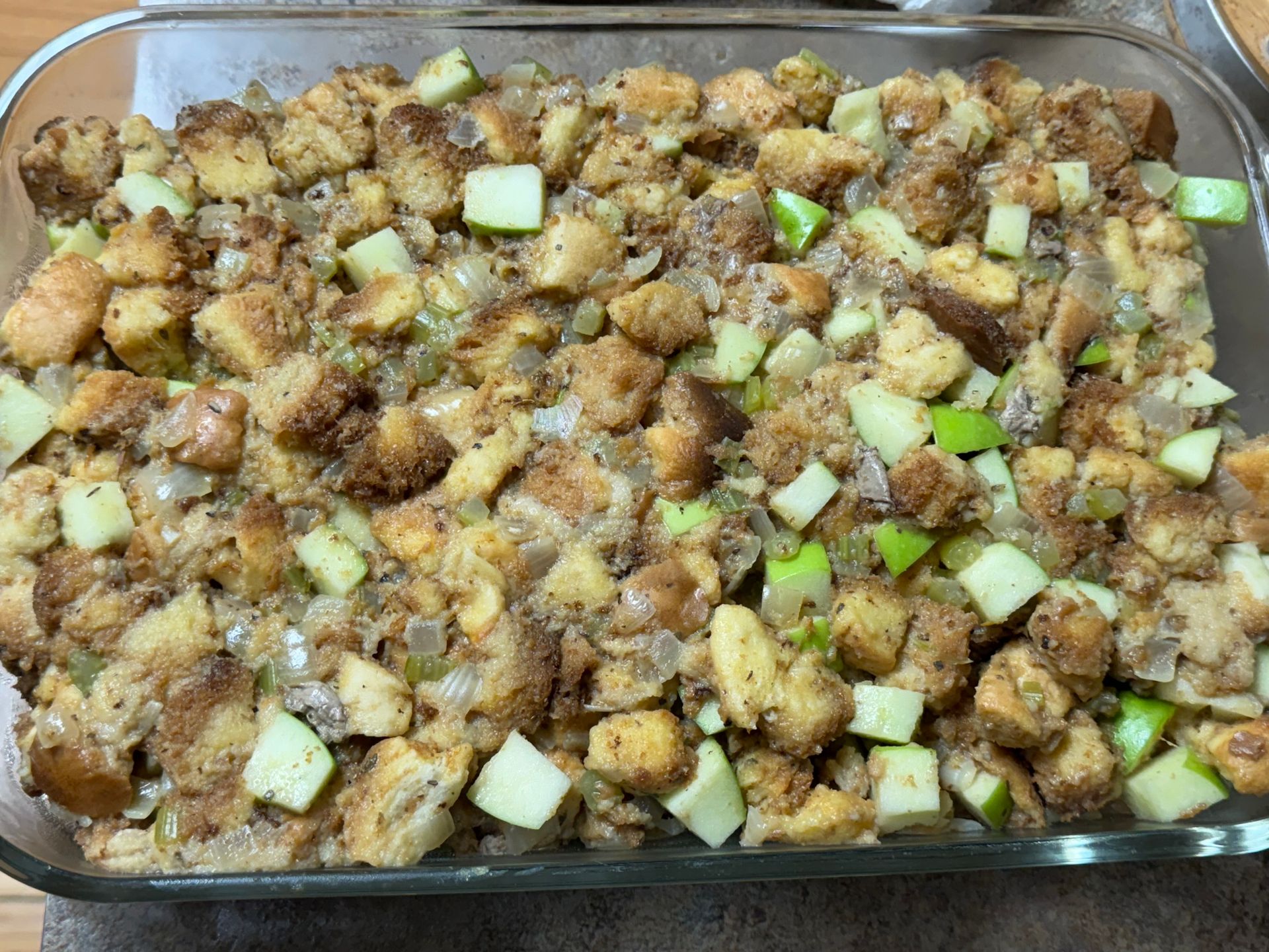 A glass casserole dish filled with stuffing and apples.