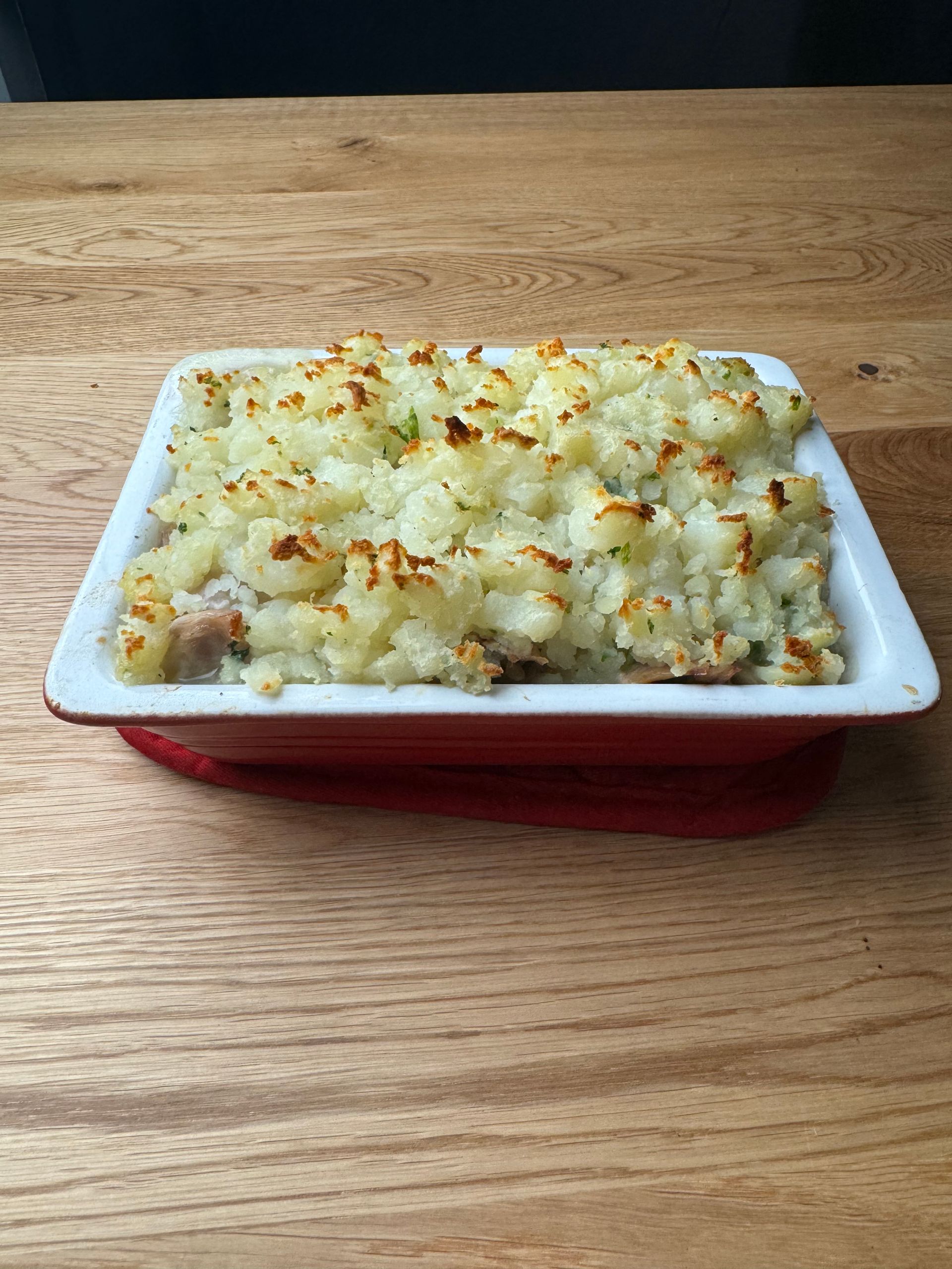 A casserole dish filled with mashed potatoes and meat is sitting on a wooden table.
