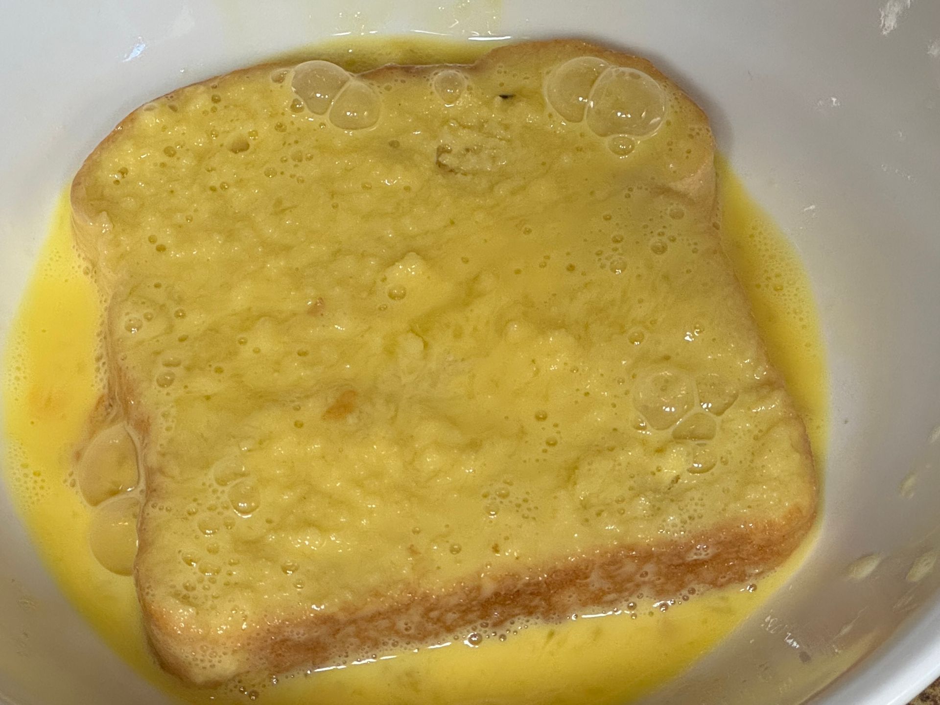A slice of french toast is dipped in a bowl of eggs.