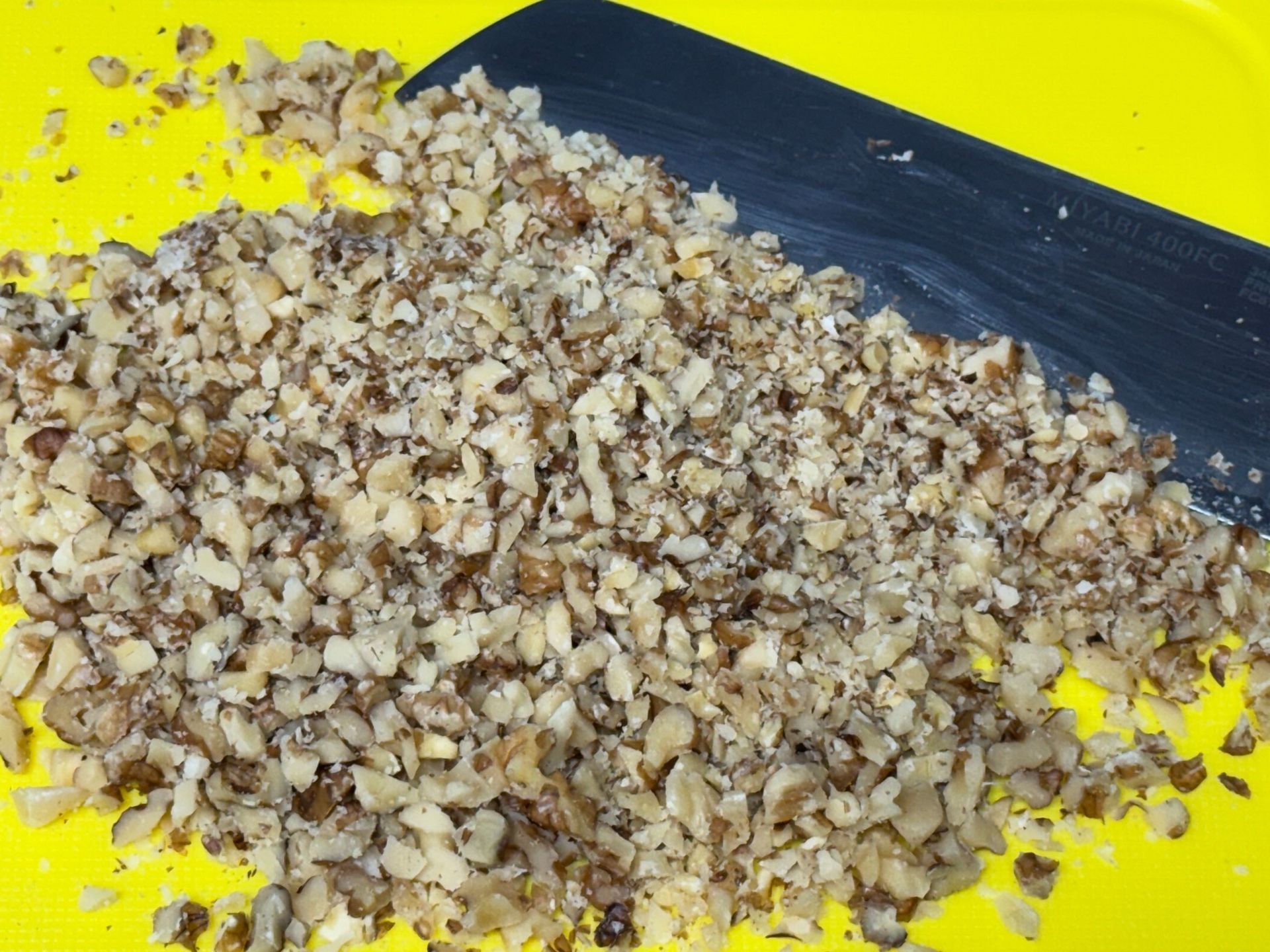 A pile of chopped nuts is on a yellow cutting board next to a spatula.