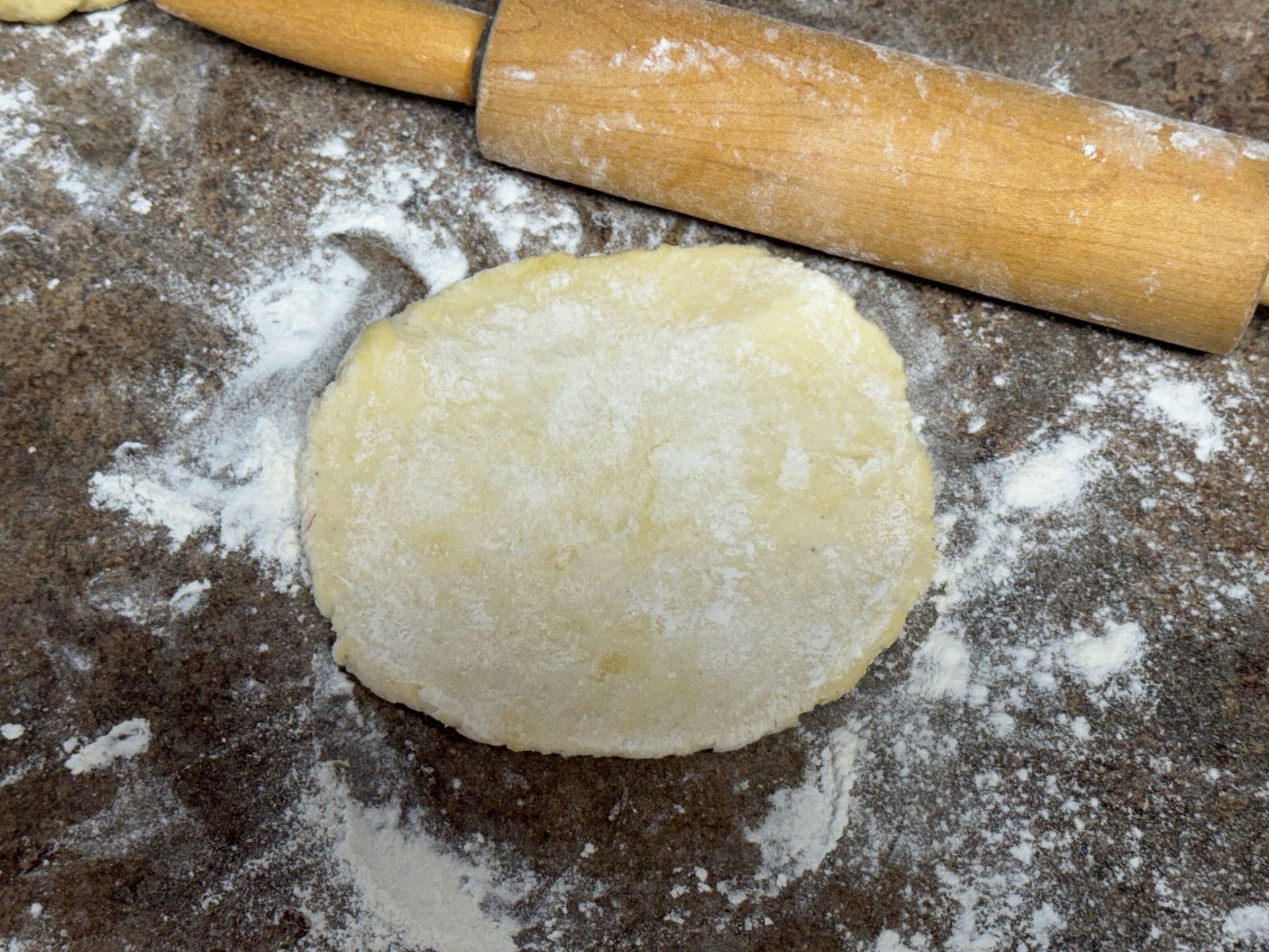 A piece of dough is sitting on a table next to a rolling pin.