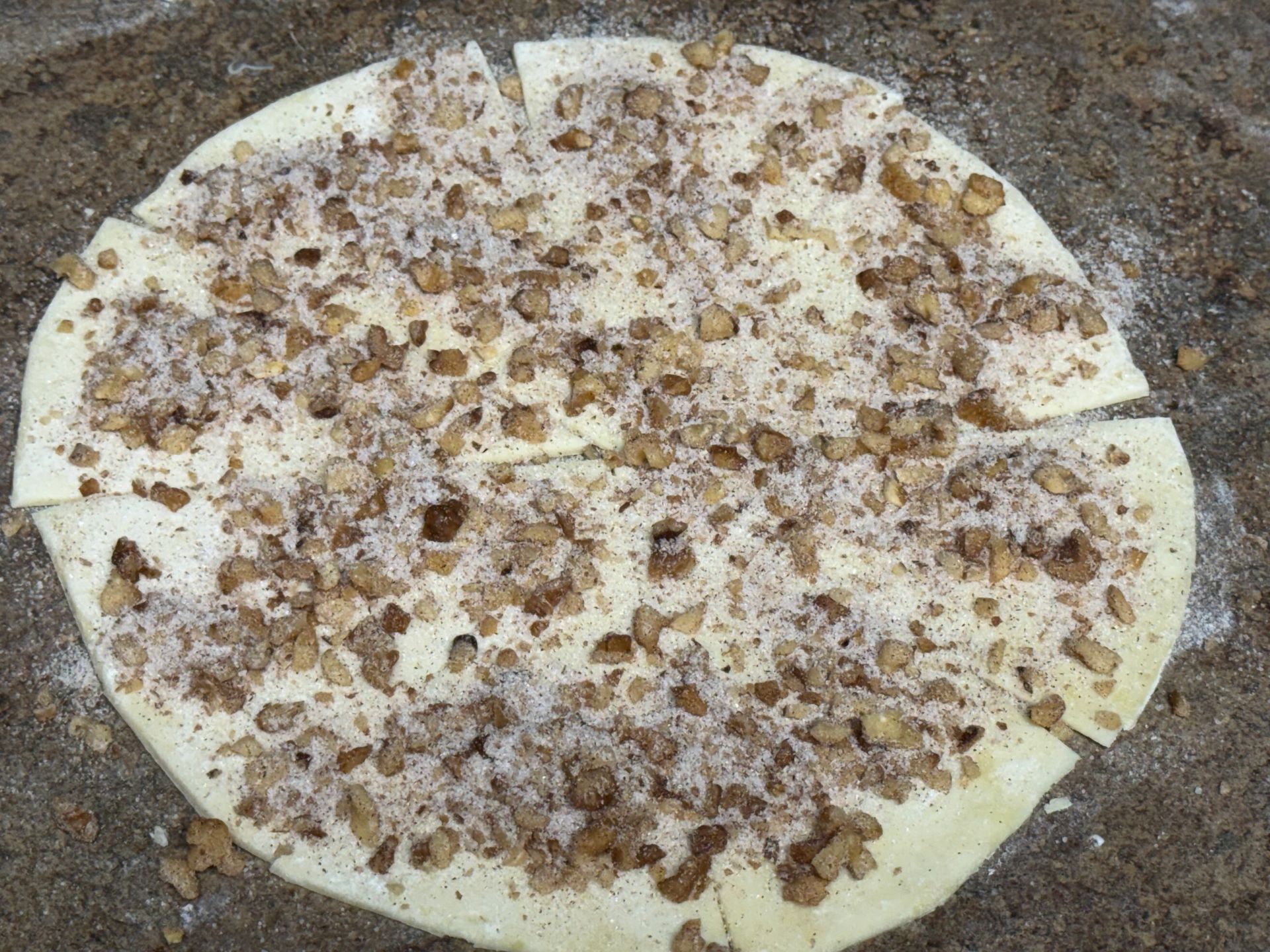 A dough circle cut into pies with nuts and cinnamon on it is sitting on a table.