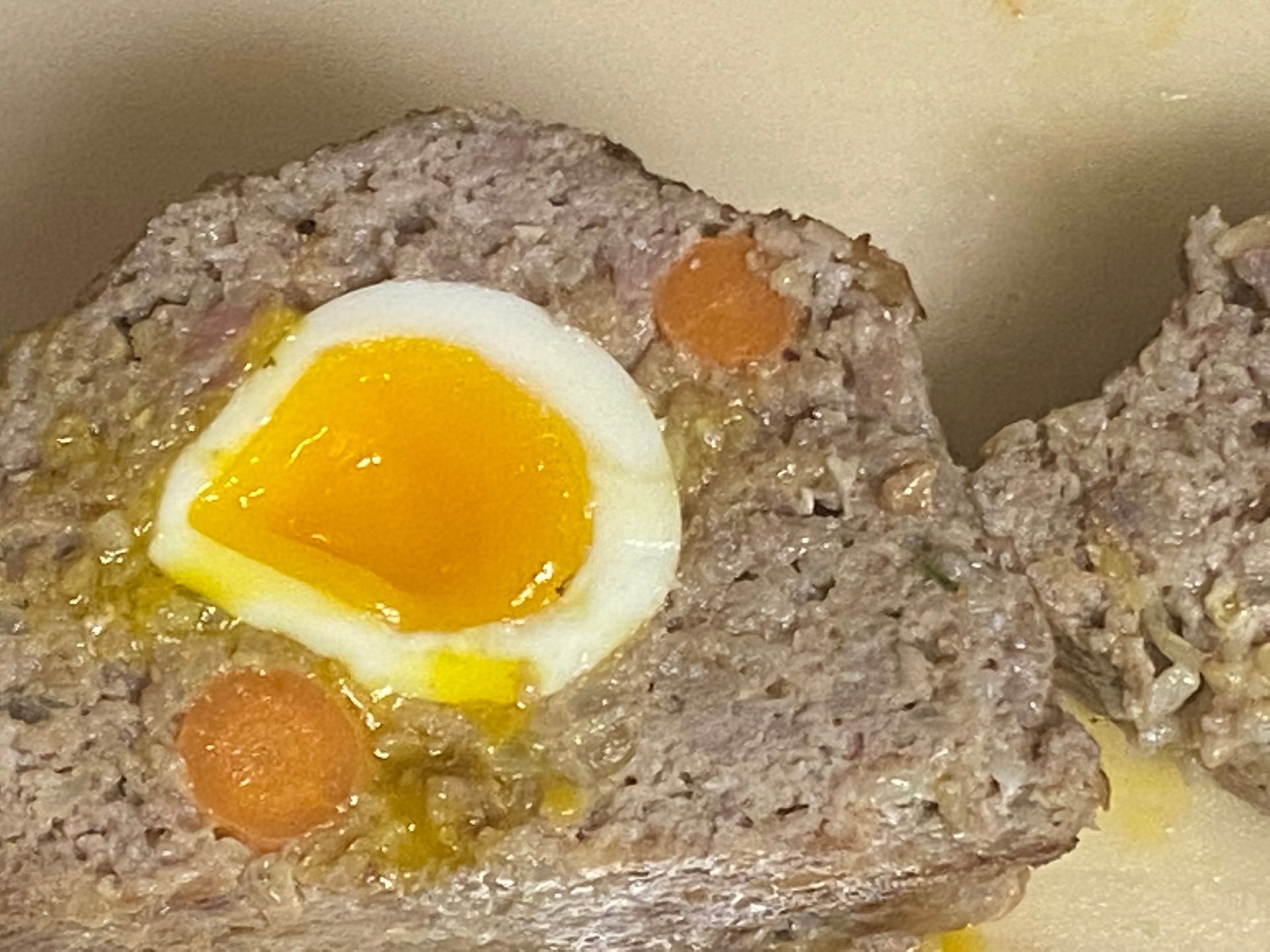 A close up of a meatloaf with eggs and carrots on a plate.