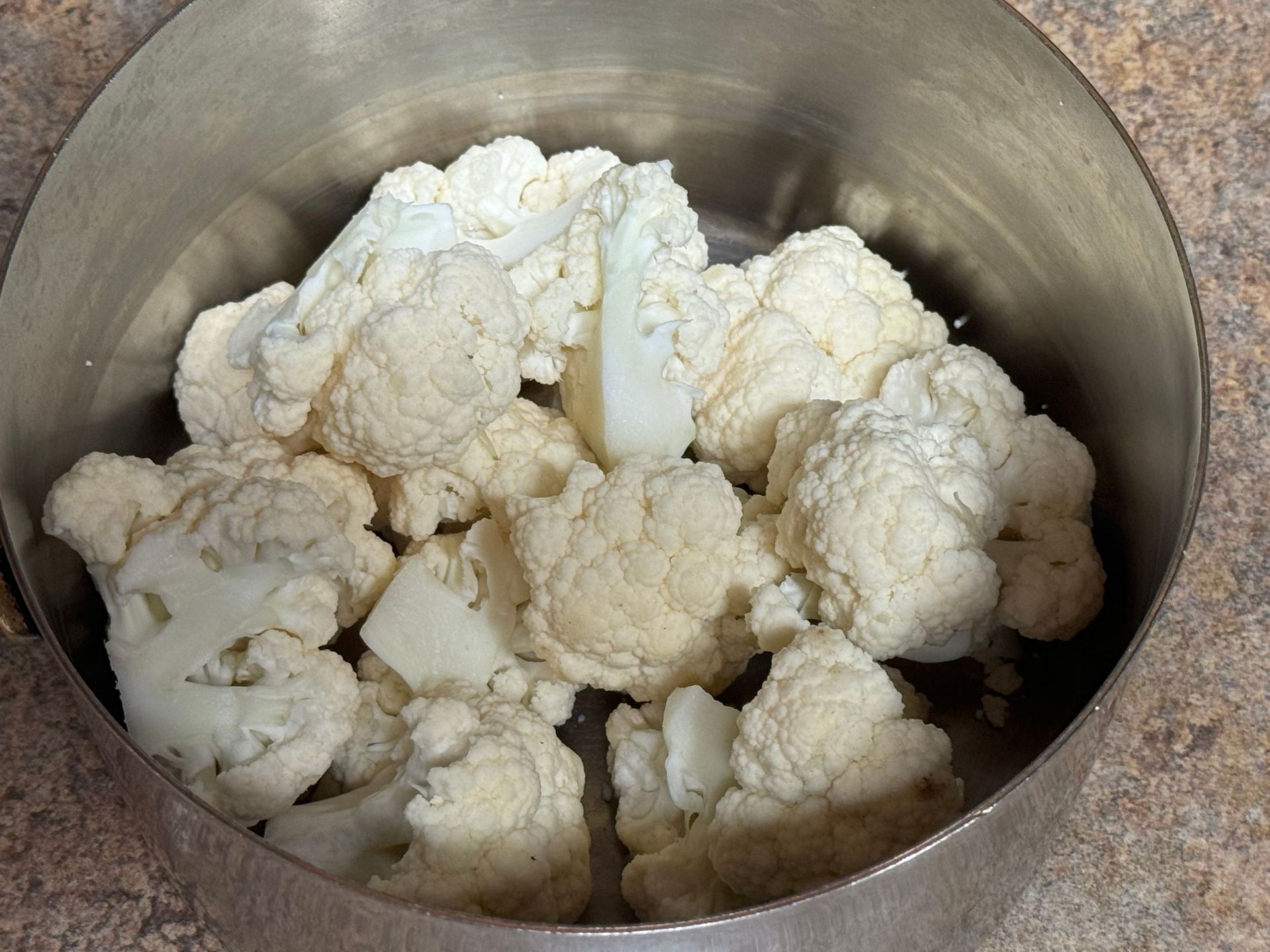 A metal bowl filled with cauliflower on a table.