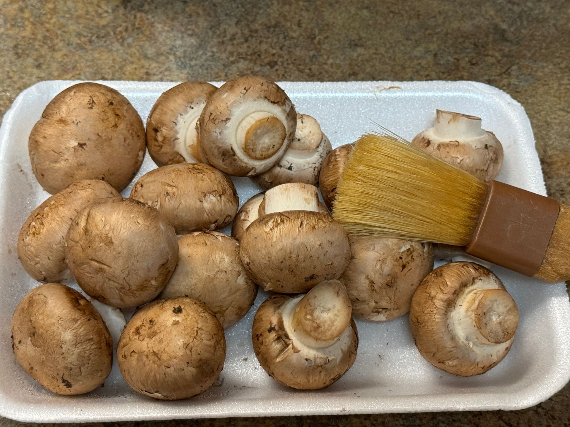A styrofoam tray filled with mushrooms and a brush.